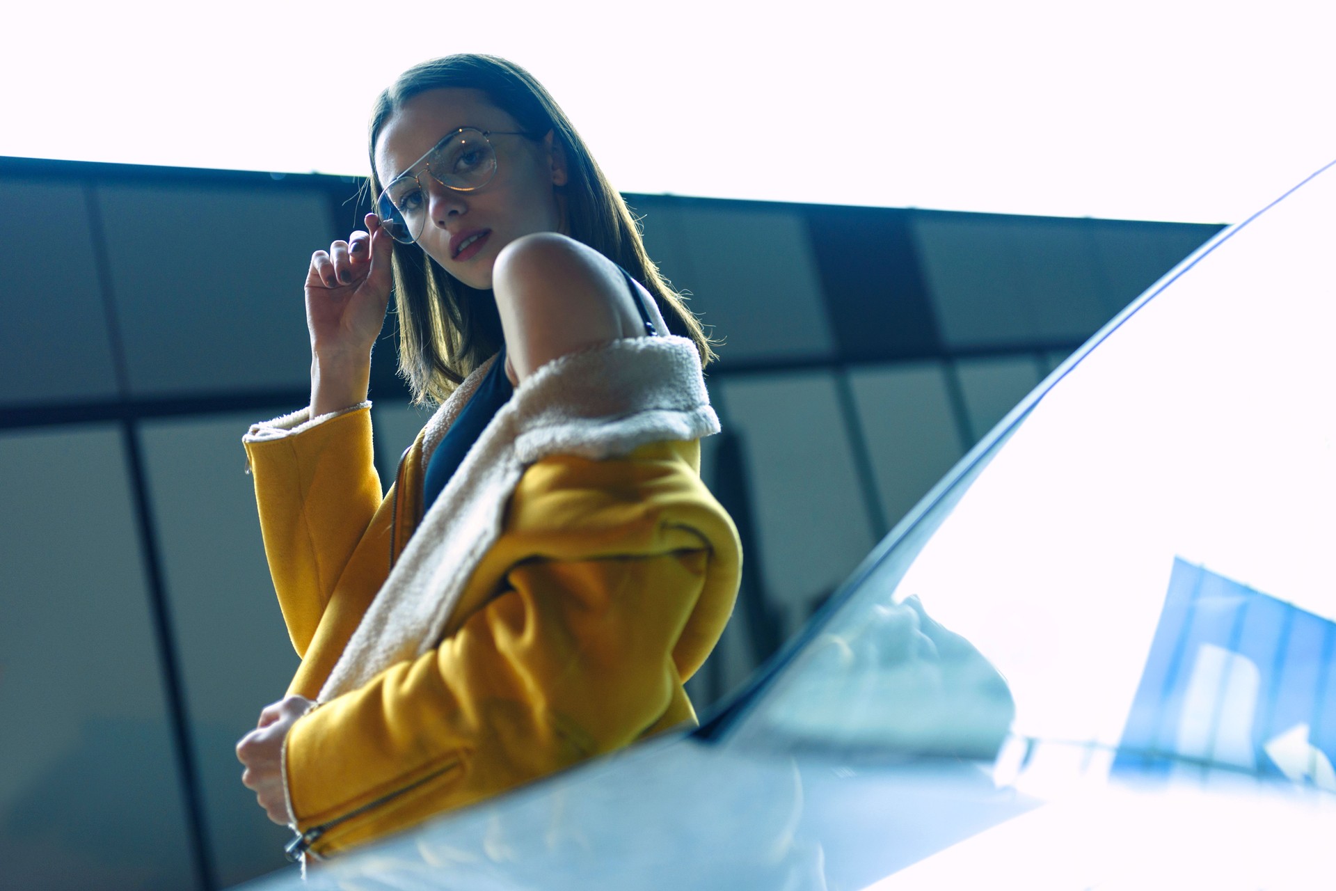 Woman in yellow jacket and glasses. City center street, lit by bright light. Womenswear fashion.