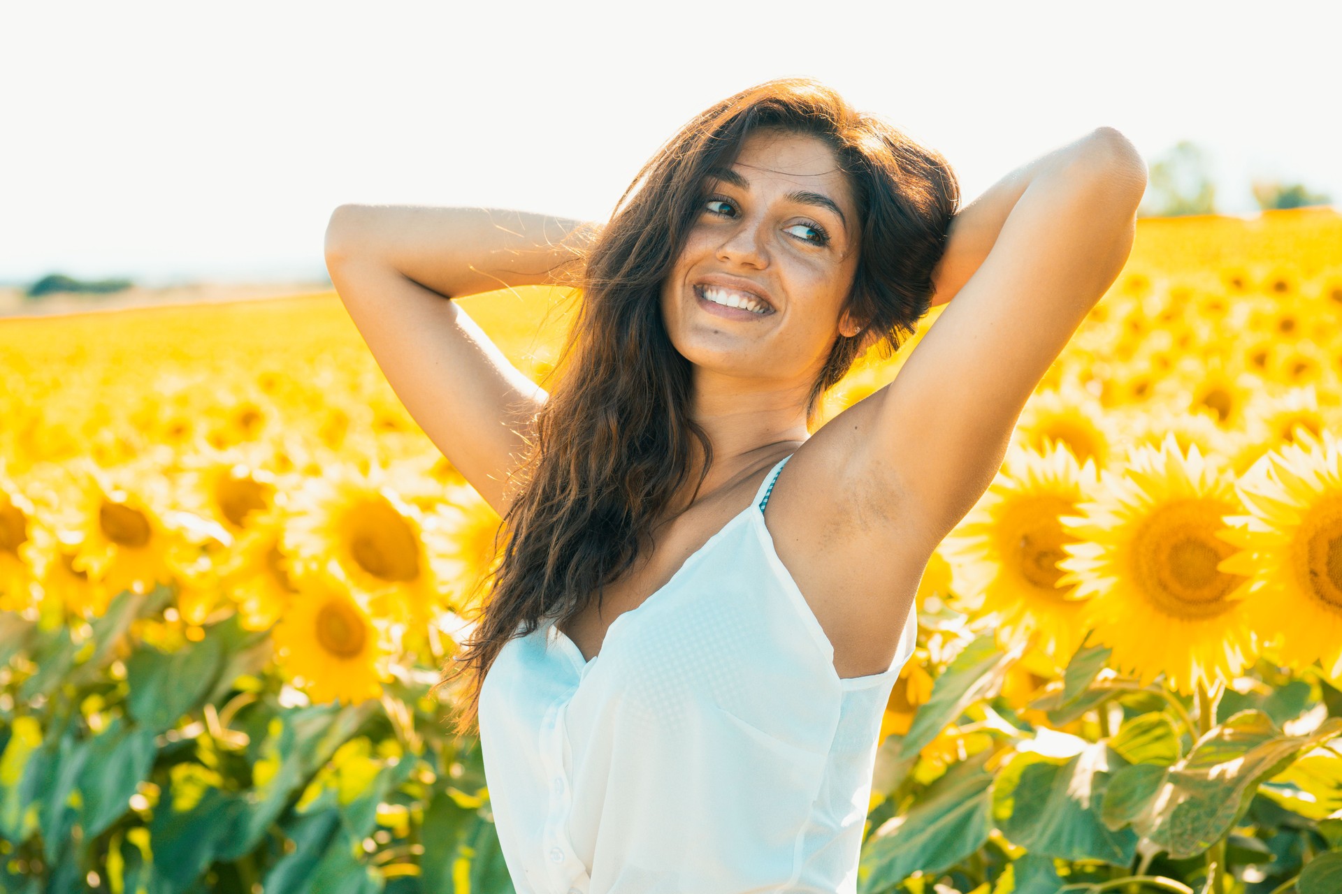 A smiling model sunbathes in a beautiful sunflower field after the pandemic ends. Perfect for summer campaign